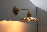 Side-angled brass scalloped disc wall light with warm glowing bulb and decorative shadow effect.