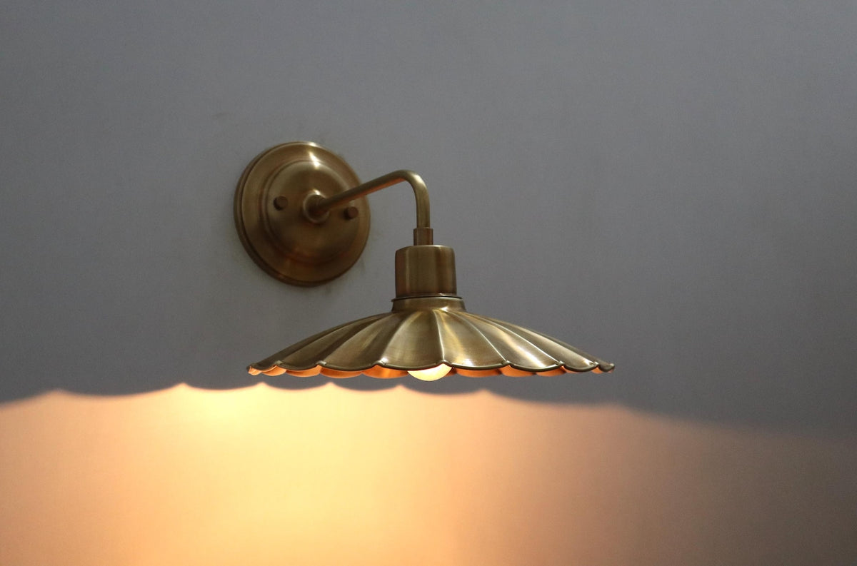 Side-angled brass scalloped disc wall light with warm glowing bulb and decorative shadow effect.