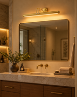 Brisbane polished brass linear wall light installed above a large bathroom vanity mirror with marble countertop, wooden cabinetry, and warm lighting.