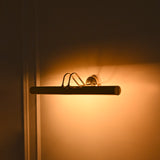 Angled night view of Brisbane polished brass picture light displaying warm ambient illumination and elegant curved metal supports.