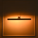 Brisbane 4 light brass linear picture light illuminated at night, casting a warm amber glow across a decorative paneled wall.