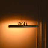 Perspective view of Brisbane 4 light linear brass picture light with elongated cylindrical shade and soft amber lighting.
