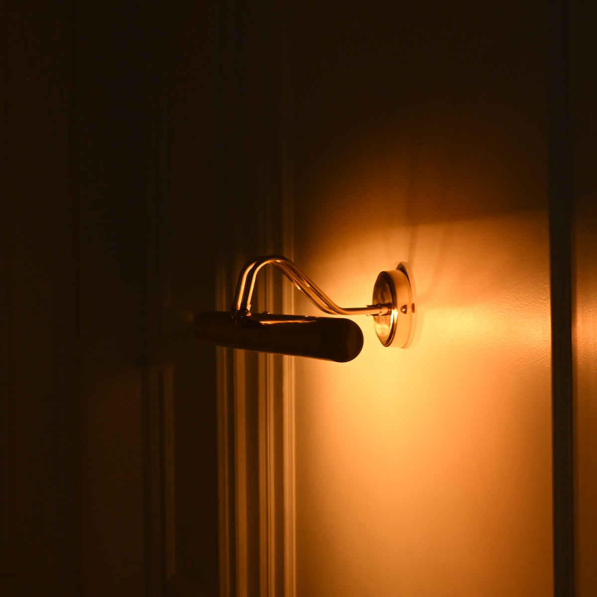 Side view of Brisbane brass wall picture light at night highlighting the curved mounting arm and warm golden wall illumination.