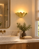 Brooklyn polished brass ruffled wall sconce installed above a marble bathroom vanity with a brass-framed mirror, warm accent lighting, and elegant contemporary decor.