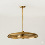 Brushed brass disc chandelier suspended from ceiling, showcasing sculpted form and soft uplighting.