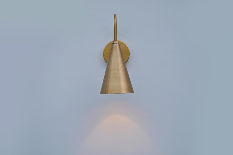 Handmade brushed brass cone wall sconce showing side angle with smooth satin finish and warm downward lighting.