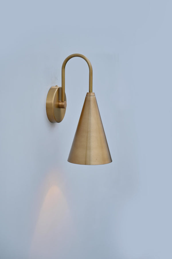Handmade brushed brass cone wall sconce showing side angle with smooth satin finish and warm downward lighting.