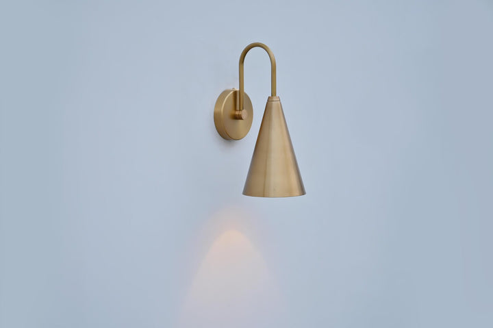Elegant brushed brass cone wall lamp mounted on wall, showing refined silhouette and smooth finish.