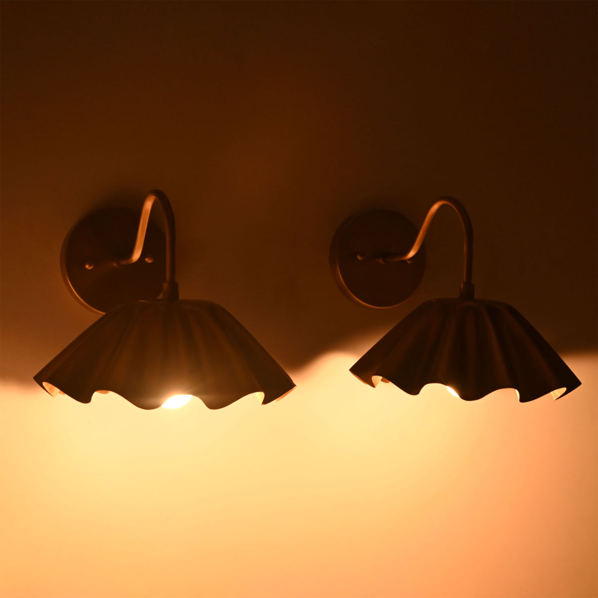 Cambria pleated brass wall sconces illuminated with warm ambient light creating soft downward illumination beneath the scalloped shades.