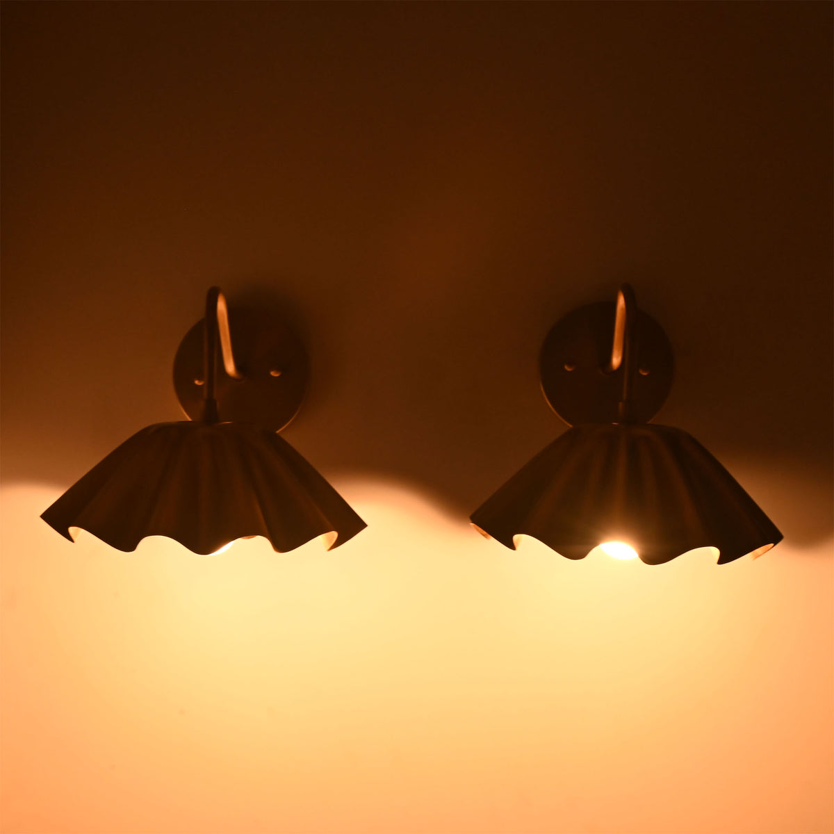 Front view of illuminated Cambria brass wall sconces with handcrafted pleated shades casting a warm ambient glow.