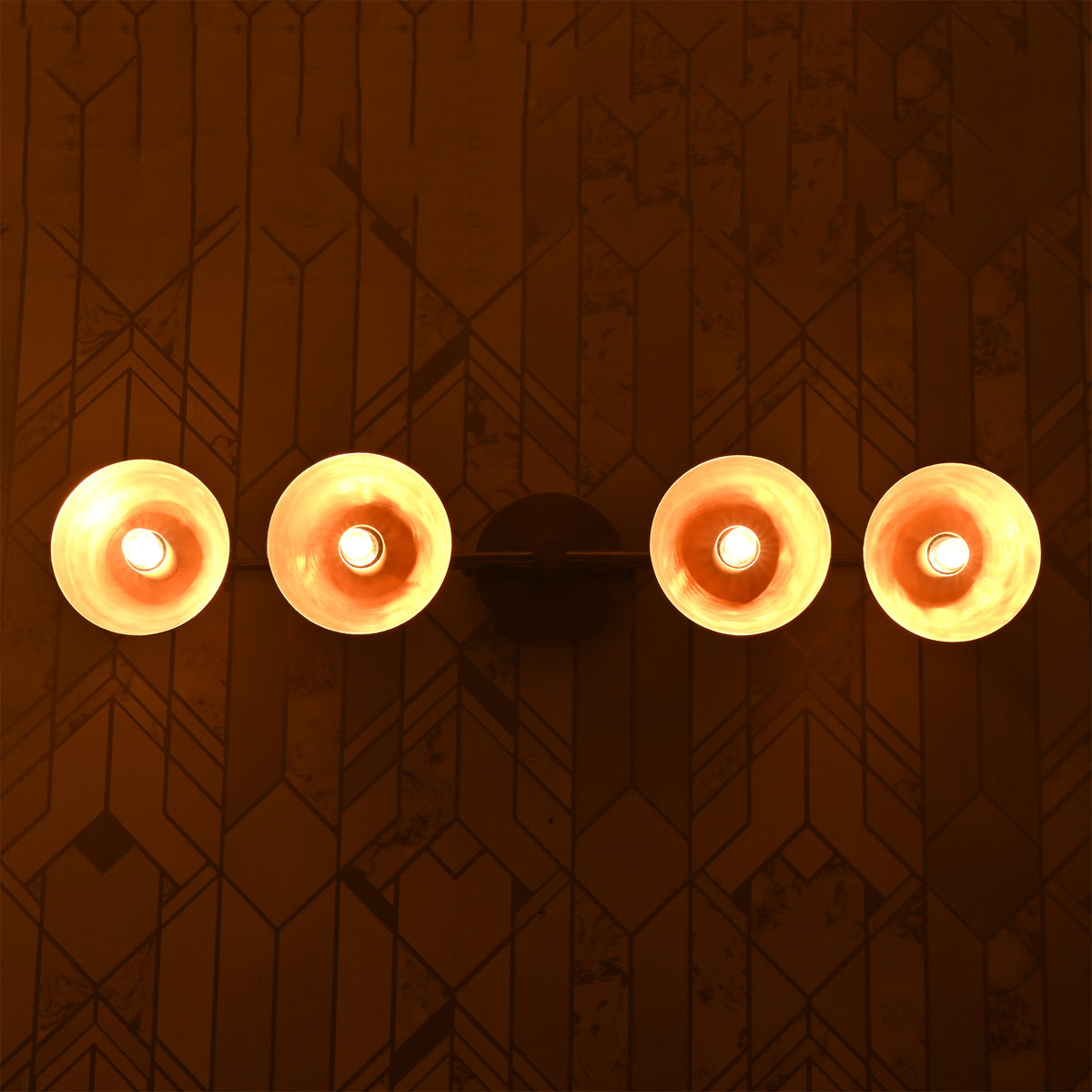 Capri Disc Linear Wall Light glowing warmly with four round disc shades on a patterned wall.