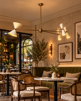 Catania 8-light sculptural ivory cone chandelier illuminating an elegant contemporary café with olive-green banquette seating, marble tables, woven chairs, and warm atmospheric lighting.
