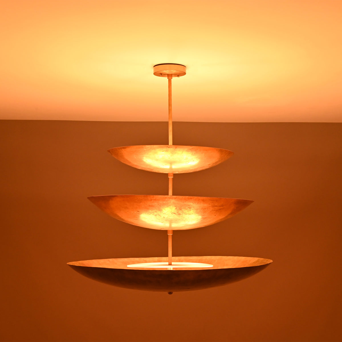 Celeste Triple Saucer Pendant Light glowing warmly in low light with dramatic layered ambient lighting effect.