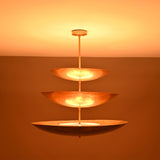 Celeste Triple Saucer Pendant Light glowing warmly in low light with dramatic layered ambient lighting effect.