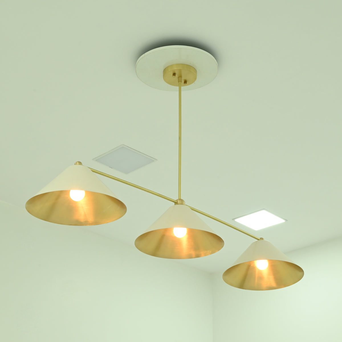 Angled view of Charleston 3-light chandelier featuring ivory cone shades, brass arms, and warm glowing bulbs.