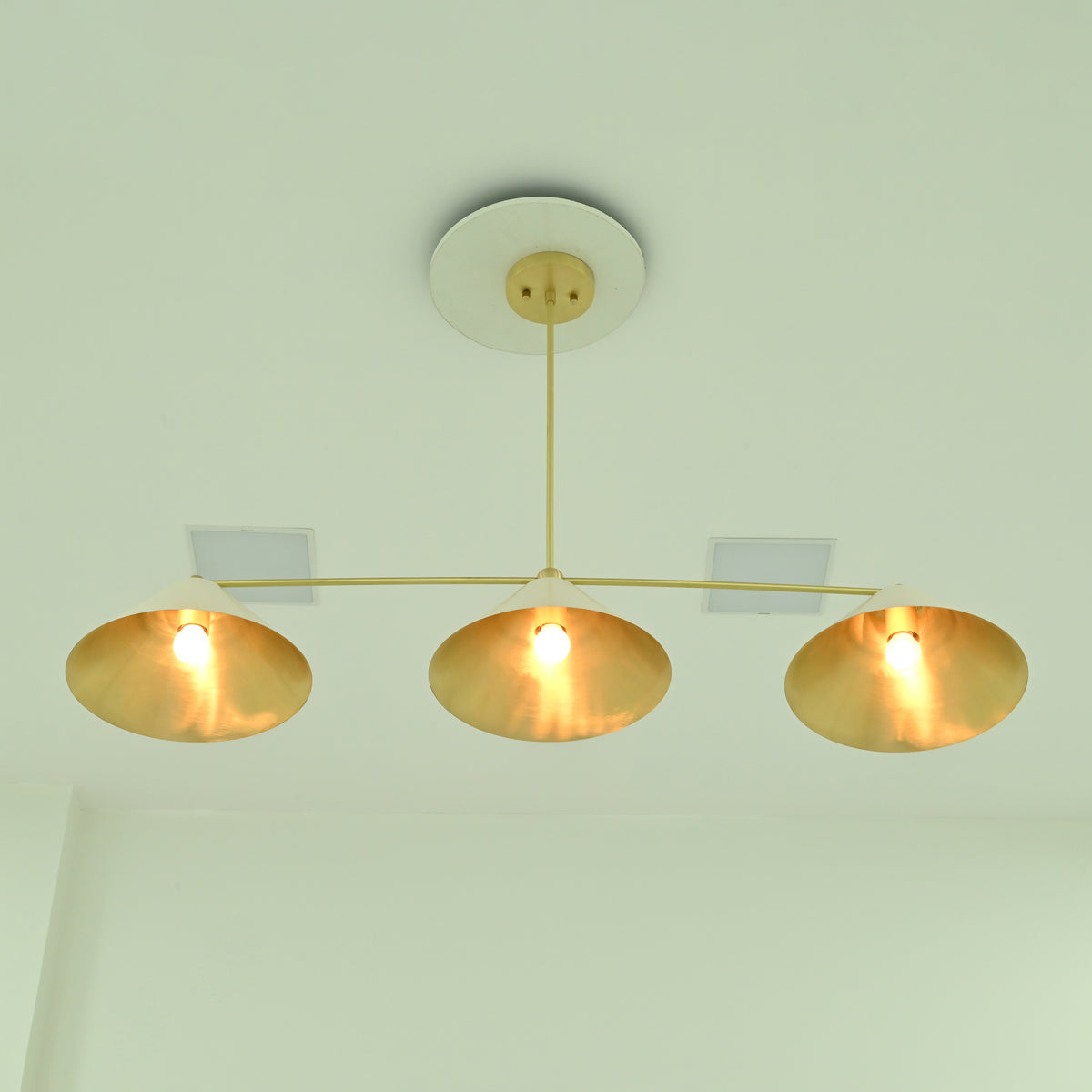 Bottom view of Charleston three-light chandelier showcasing wide conical shades, reflective gold interiors, and illuminated bulbs.