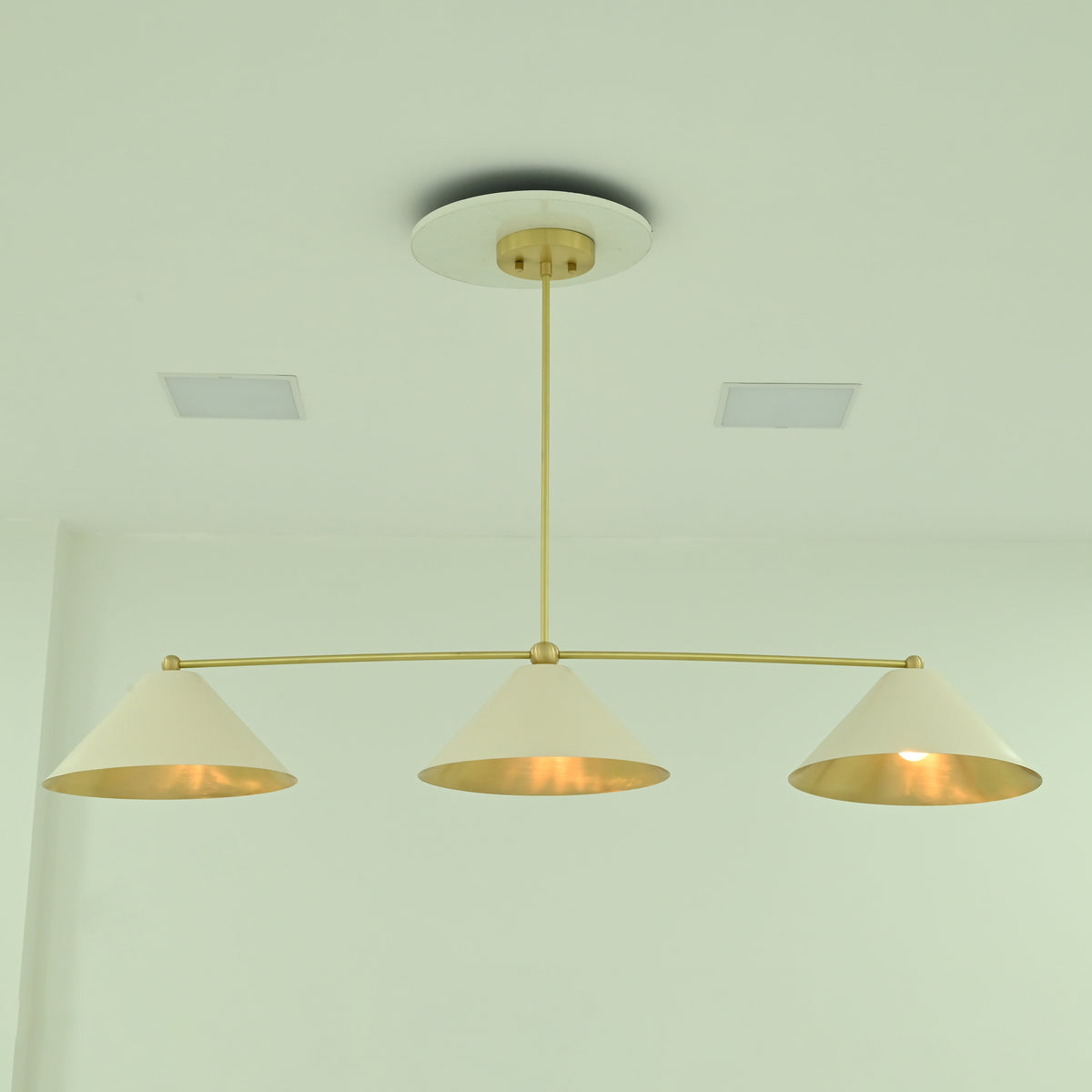 Front view of Charleston 48-inch linear chandelier featuring three evenly spaced ivory cone shades with warm interior lighting.