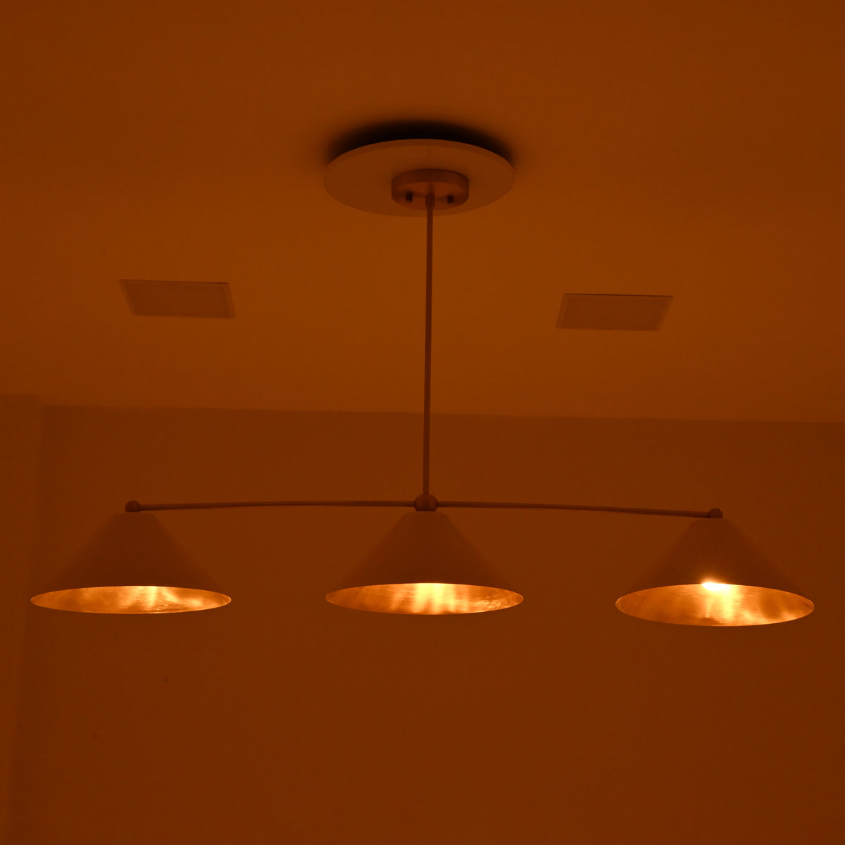 Charleston modern three-light chandelier displaying soft golden light from ivory cone shades in a moody evening setting.