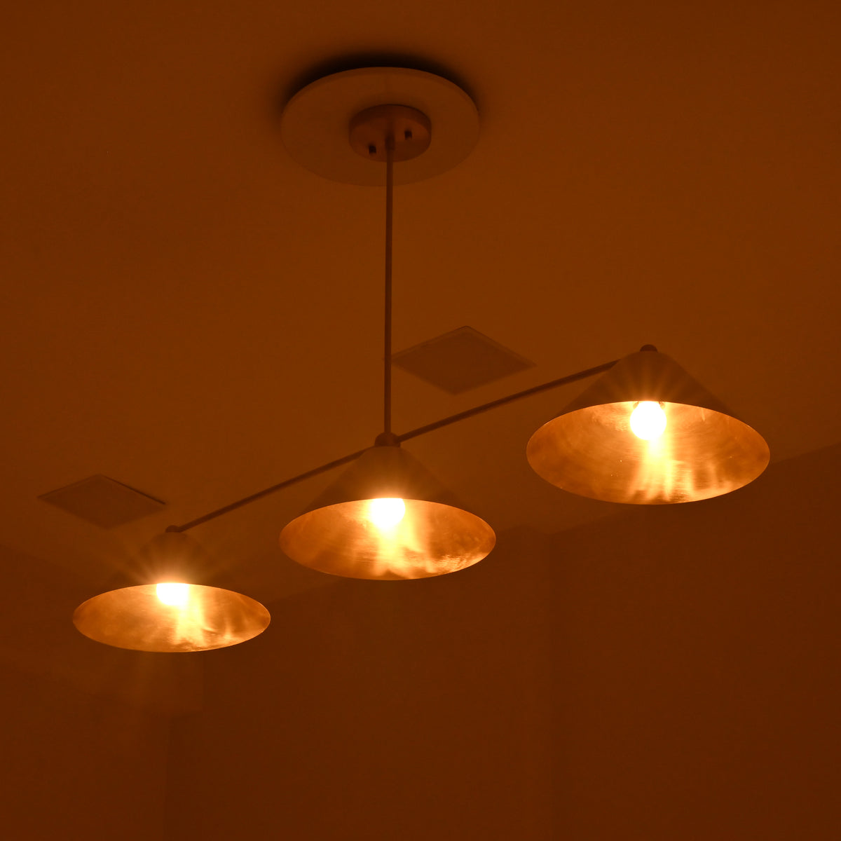 Charleston brass and ivory cone chandelier illuminated in a dark interior, creating a rich golden ambient glow.