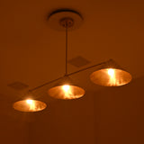 Charleston brass and ivory cone chandelier illuminated in a dark interior, creating a rich golden ambient glow.