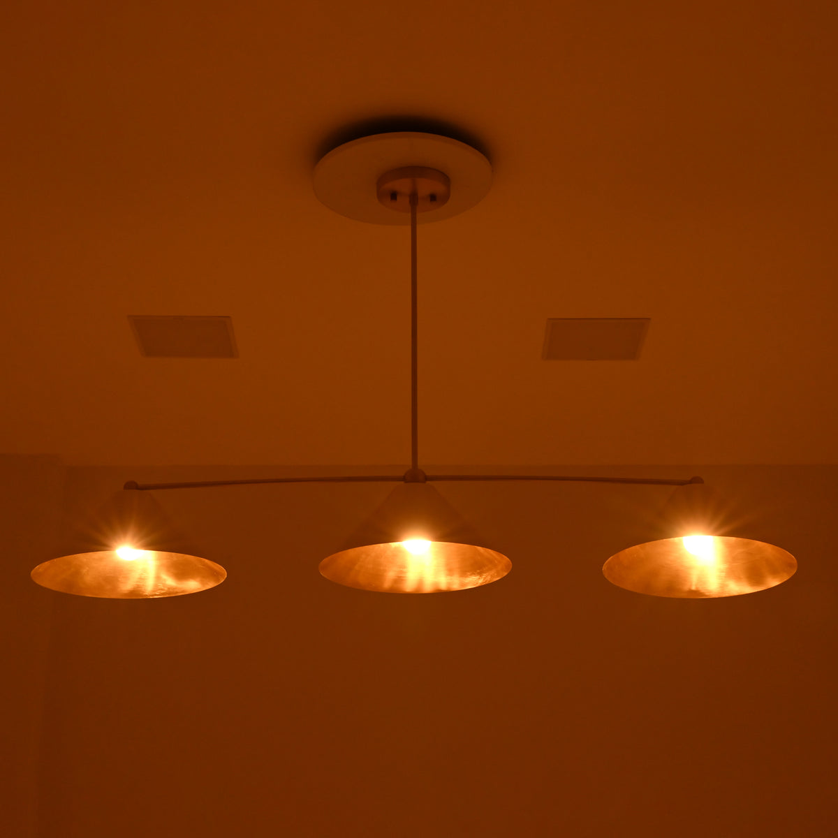 Front night view of Charleston 3-light linear chandelier with warm golden illumination beneath three conical metal shades.