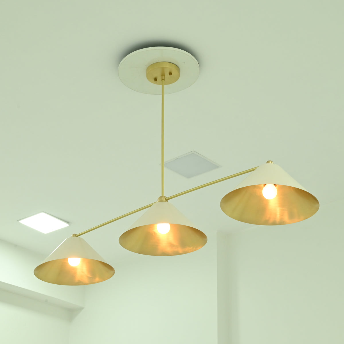 Charleston modern linear chandelier with three downward-facing ivory cone shades and brass-finish horizontal arms, illuminated from below.