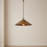 Single brass cone pendant light with chain hanging against a plain beige wall in a minimal interior.