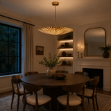 Crete 5 light brass fluted bowl chandelier illuminated above a round dining table in an elegant warm modern dining room.