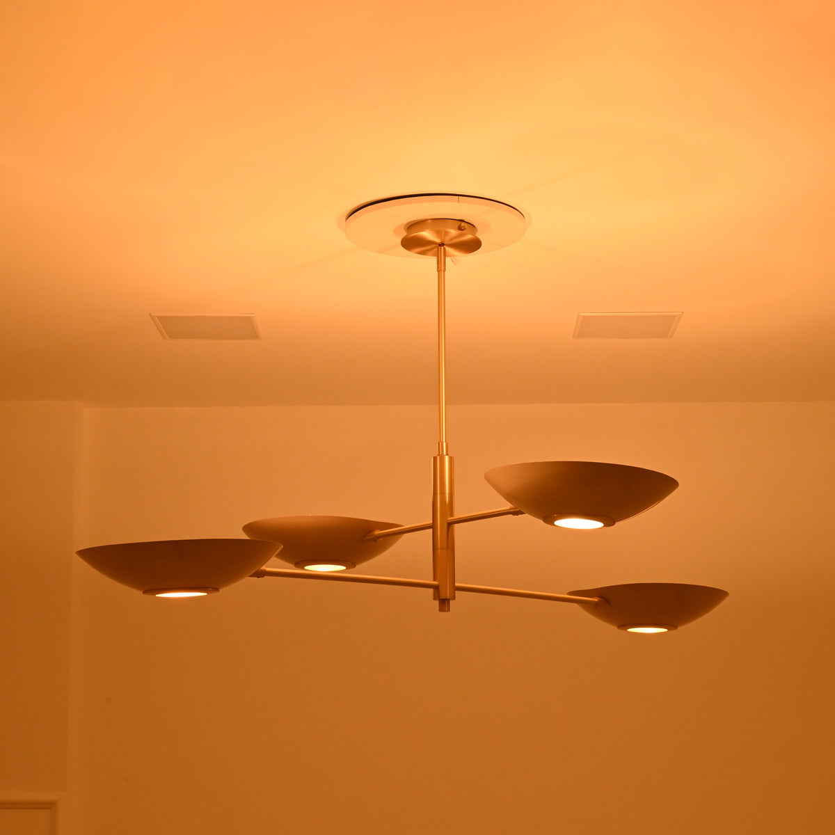 Dallas four-bowl sculptural ceiling chandelier shown at an angle with illuminated circular light openings and elegant brass construction.