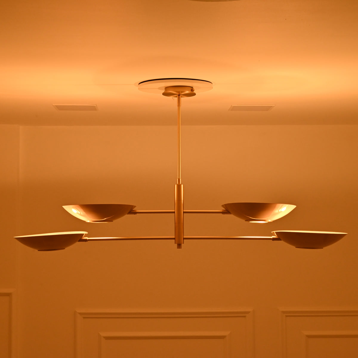 Front view of Dallas four-light linear chandelier with a brass finish, two-tier bowl arrangement, and warm ambient evening illumination.