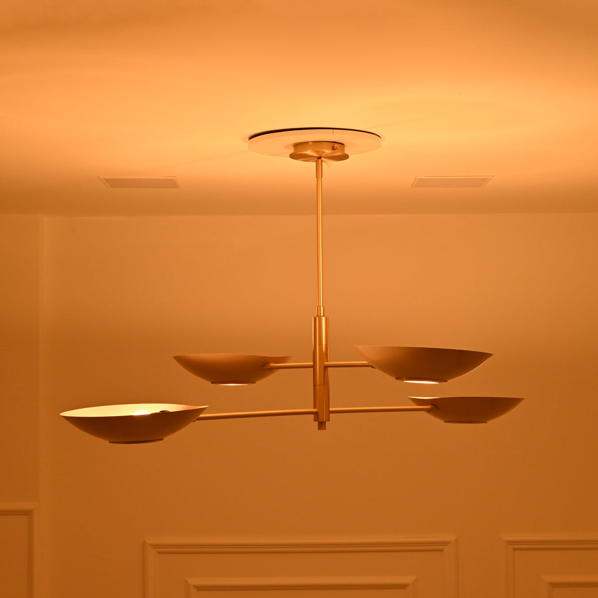 Side-angle view of Dallas 4-light brass chandelier highlighting its slim horizontal arms, staggered bowl shades, and warm decorative glow.