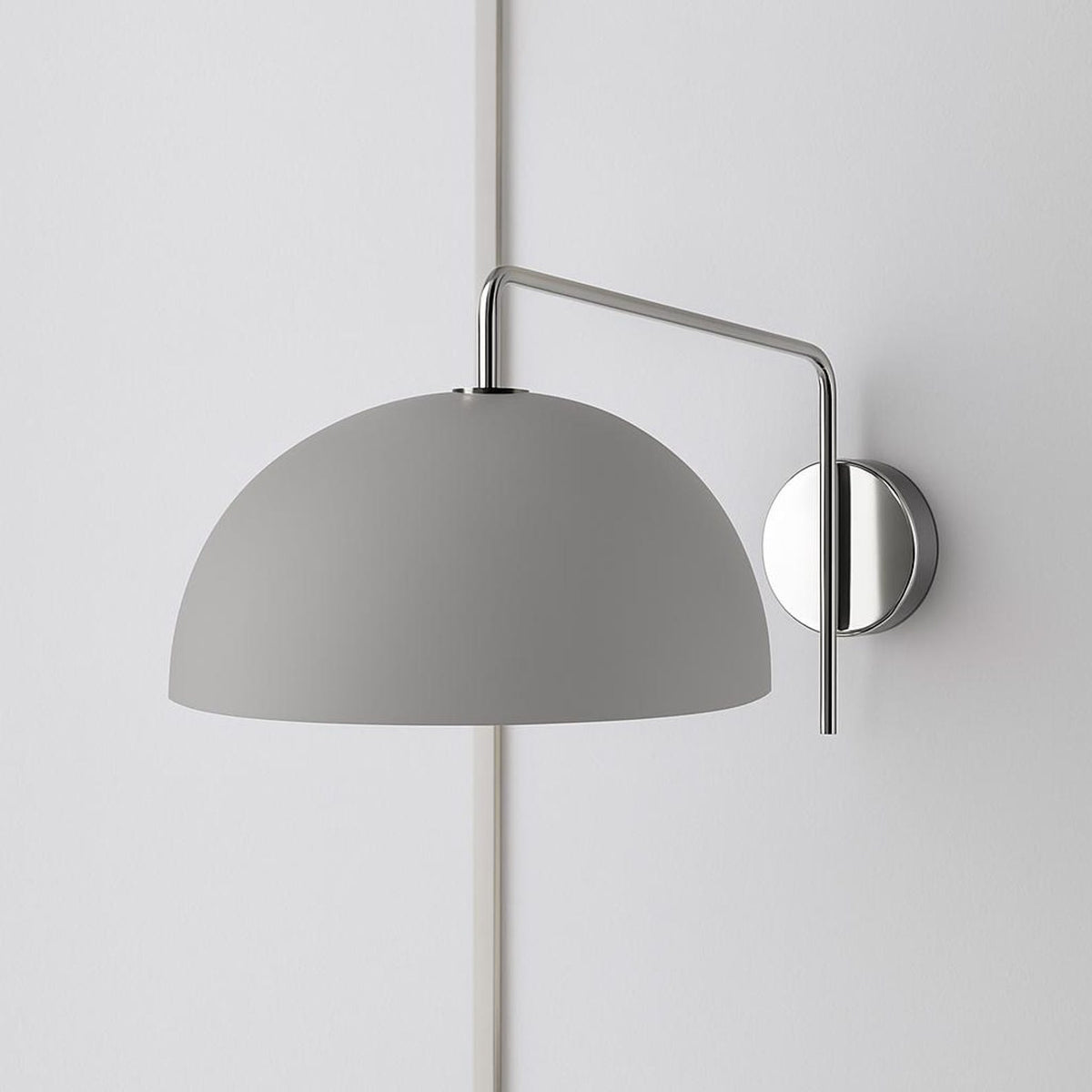 Polished chrome swing-arm wall sconce with matte gray dome shade mounted on a pale wall.