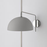 Polished chrome swing-arm wall sconce with matte gray dome shade mounted on a pale wall.
