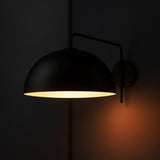 Matte black dome wall sconce switched on, casting warm light on a dark background.