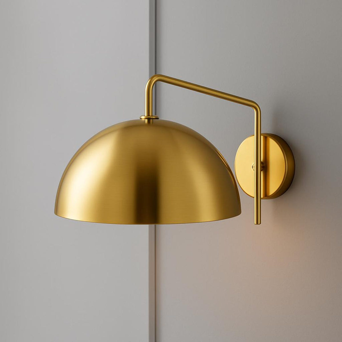 Polished brass dome wall sconce with matching brass arm and round backplate on a gray wall.