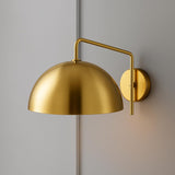 Polished brass dome wall sconce with matching brass arm and round backplate on a gray wall.