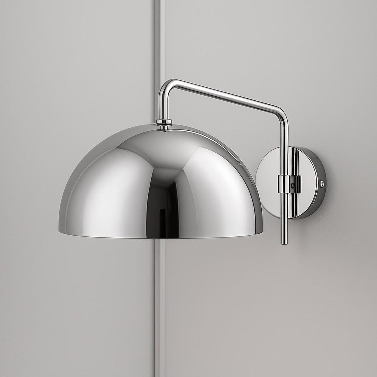 Mirror-finish chrome dome wall sconce with chrome arm and round backplate on a light gray wall.