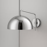 Mirror-finish chrome dome wall sconce with chrome arm and round backplate on a light gray wall.