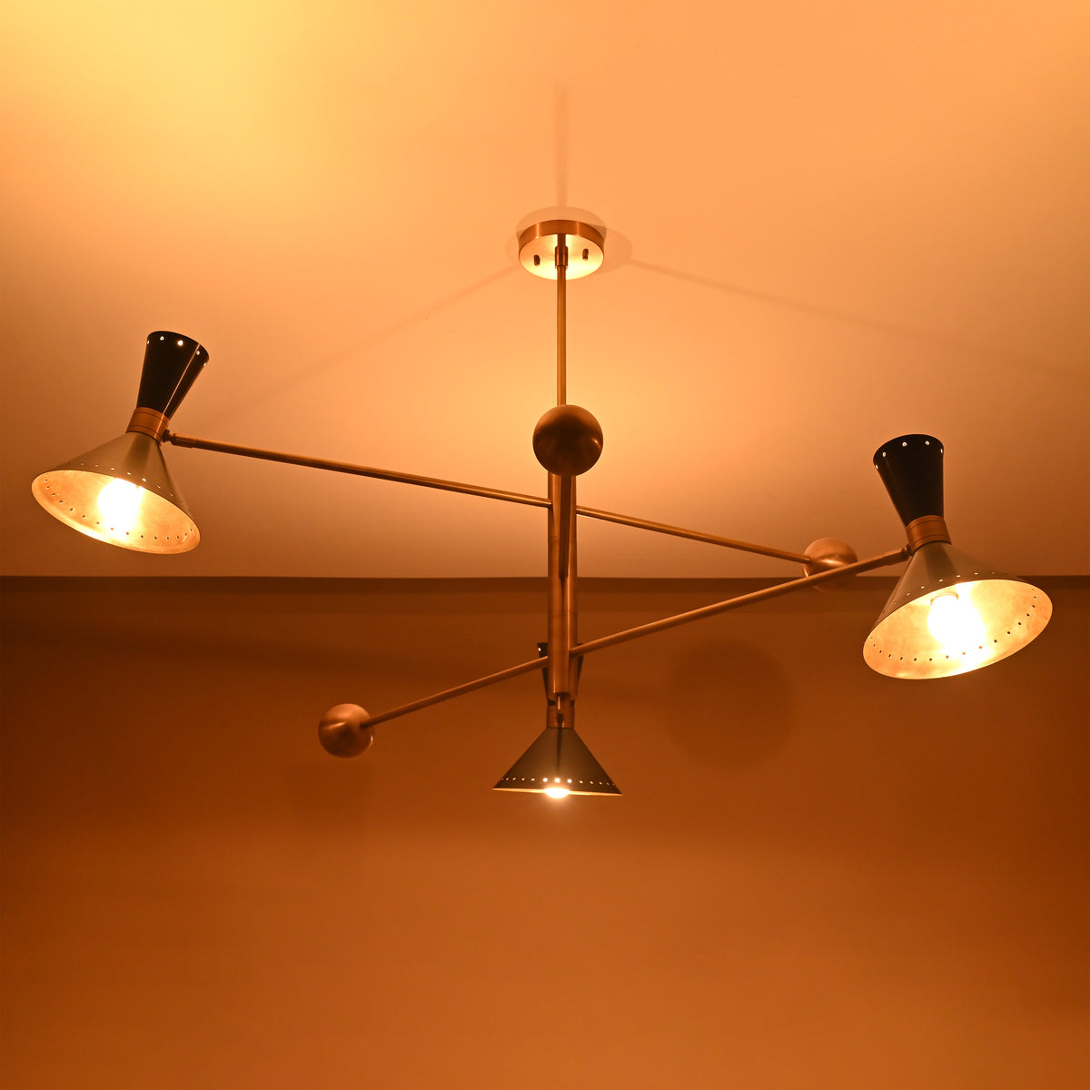 Warm overhead perspective of 6 light mid-century brass chandelier in dark setting