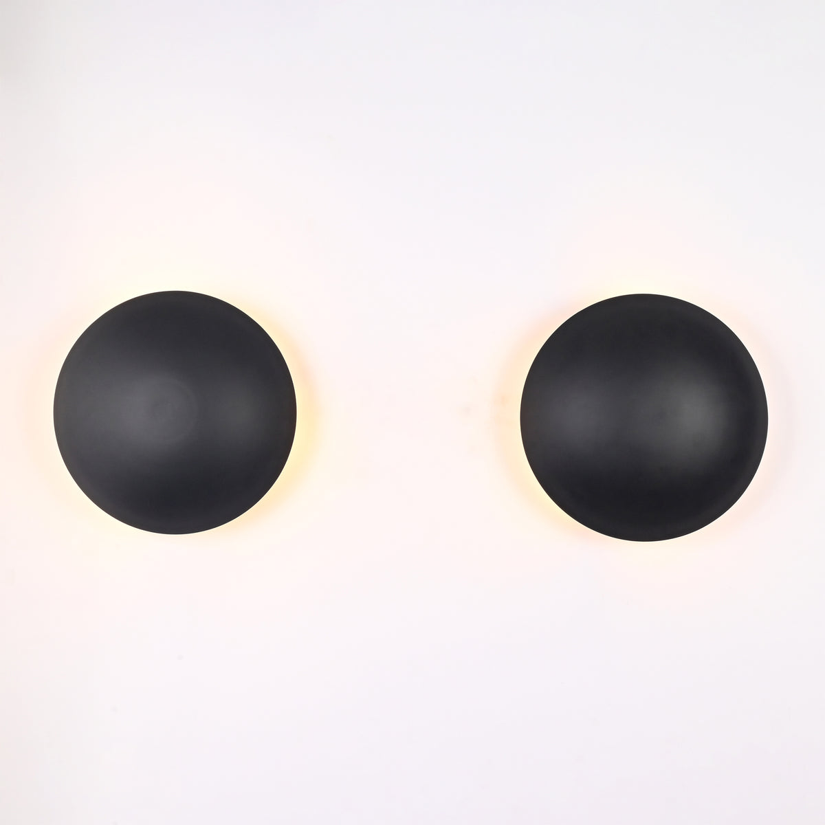 Illuminated front view of the Eclipse black dome wall sconce casting a warm halo backlight against the wall.