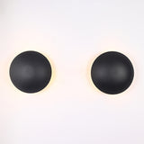 Illuminated front view of the Eclipse black dome wall sconce casting a warm halo backlight against the wall.