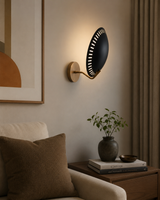 Eclipse perforated disc wall sconce illuminated in a modern living room beside an armchair with warm ambient lighting.