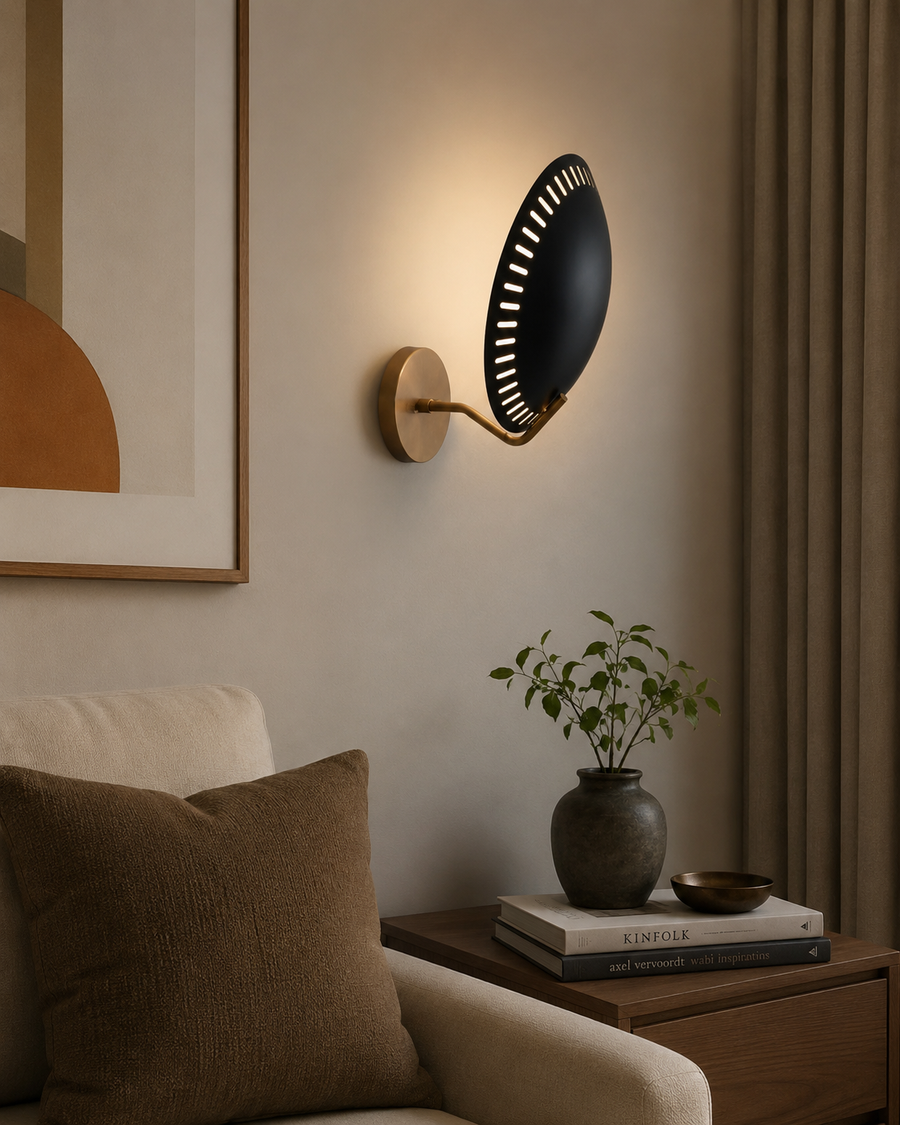 Eclipse perforated disc wall sconce illuminated in a modern living room beside an armchair with warm ambient lighting.