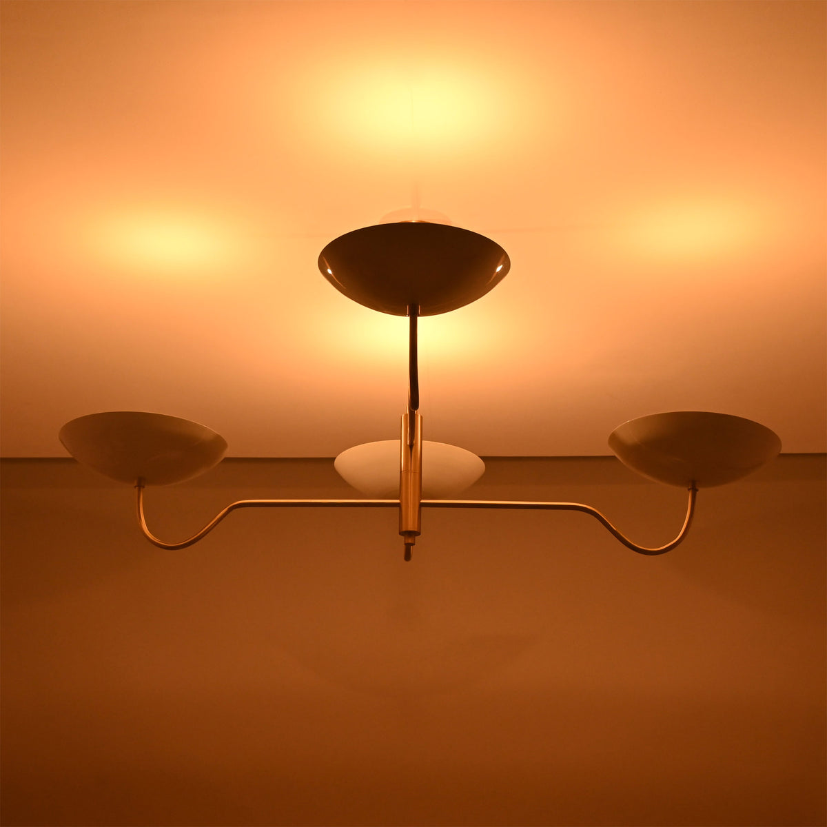 Florence Curved Arm chandelier shown illuminated, casting warm ceiling light from sculptural bowl shades.