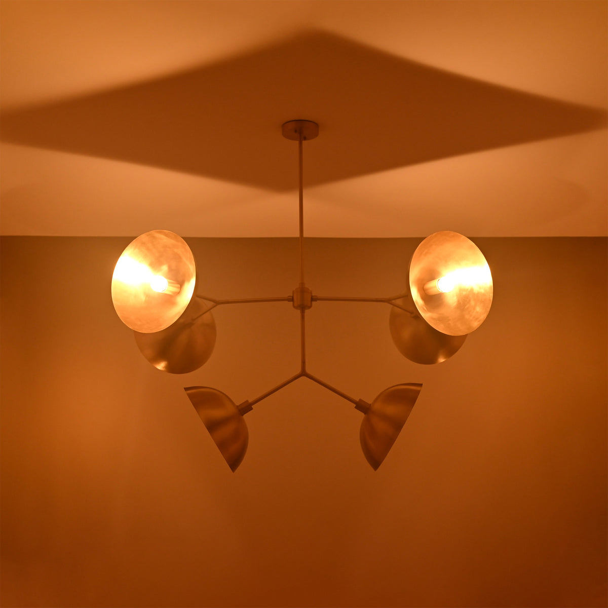 Florence Disc Orbital Chandelier installed on ceiling with four rounded shades and dramatic warm shadow pattern.