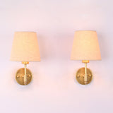 Milan natural linen shade brushed brass short wall sconce with handcrafted solid brass frame and tapered fabric shade, front view.