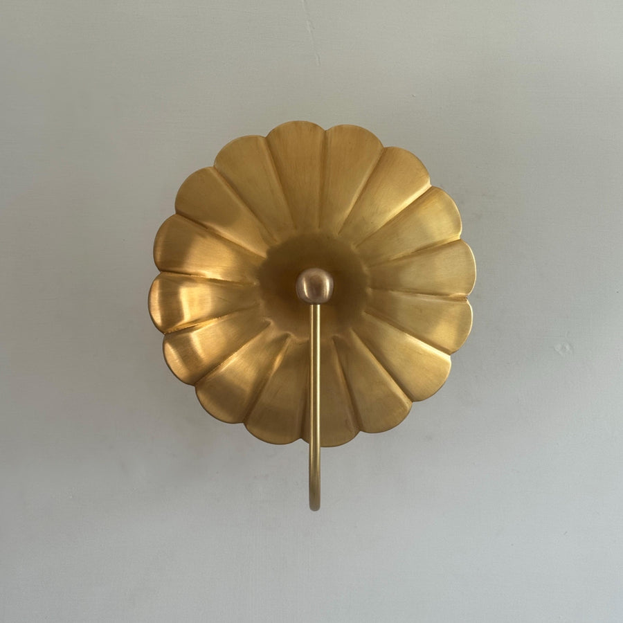 Front view of brass flower wall sconce with scalloped disc backplate and curved stem in brushed brass finish.
