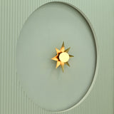 Angled view of gold starburst wall light with glowing white globe and pointed metallic rays mounted on a recessed wall.