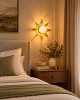 Gold starburst wall sconce installed above a walnut bedside table beside a cream upholstered bed, creating warm bedroom lighting.