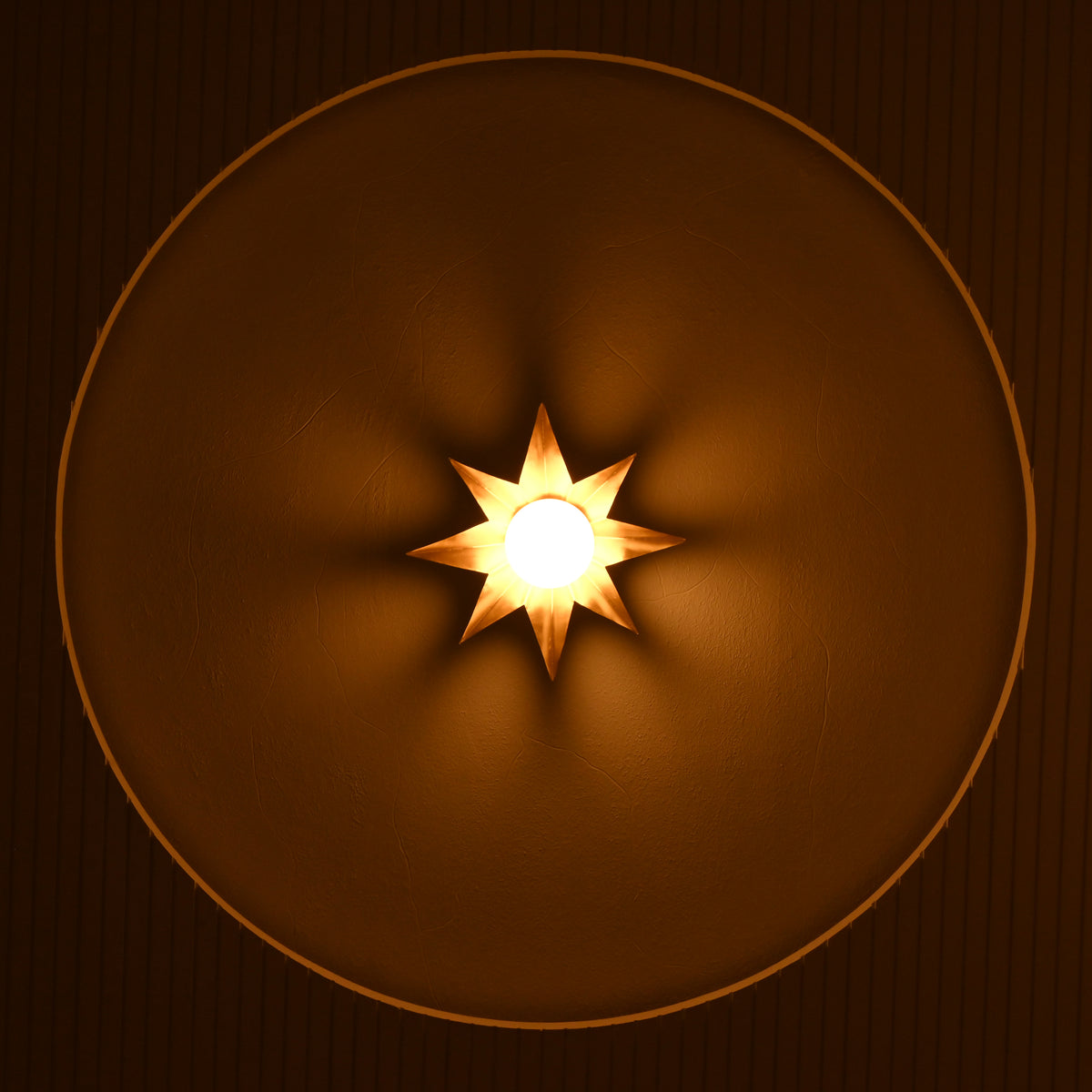 Front view of gold starburst wall sconce casting warm ambient light across a textured recessed wall.